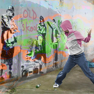A person in a hoodie, dancing hip hop in front of 'old skool' graffiti