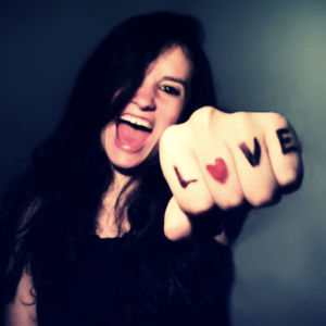 A woman laughing a showing a 'victory' fist to the camera, 'love' is written on her knuckles